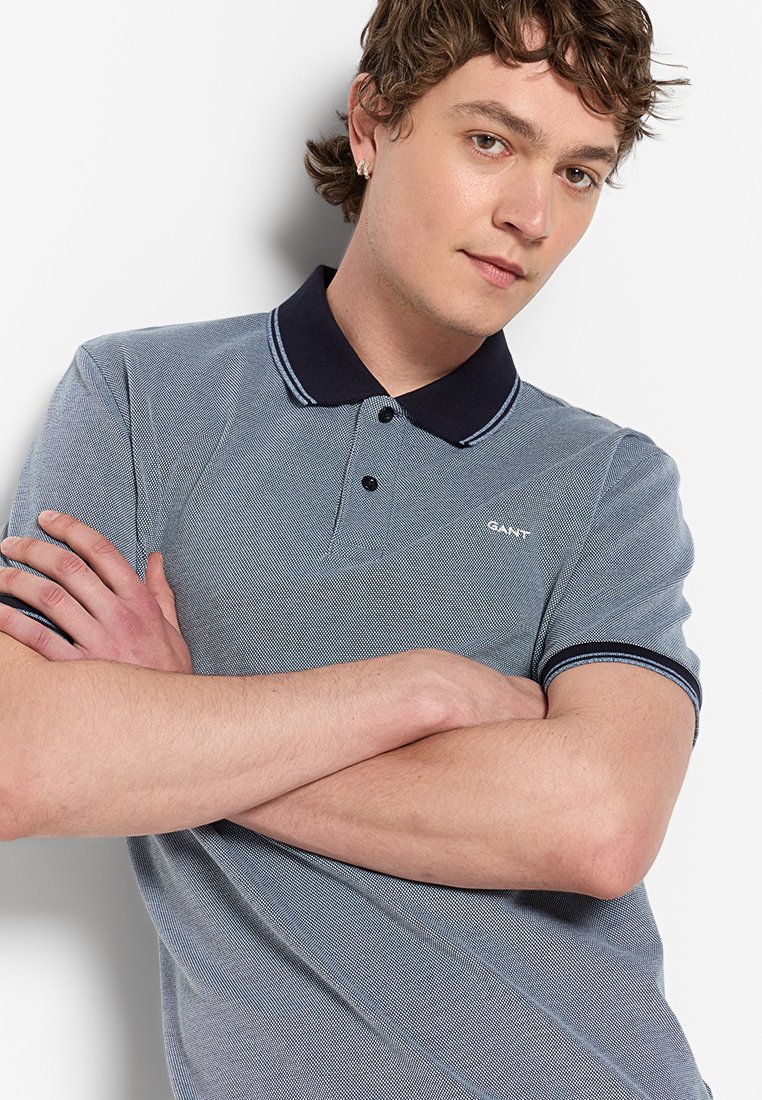 Blauw poloshirt met een gestructureerd patroon, een marineblauwe kraag en accenten op de mouwen, voorzien van een klein geborduurd logo op de linkerkant van de borst.