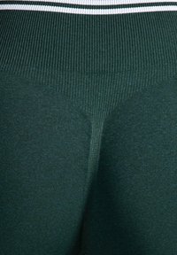 Mörkgröna ribbstickade leggings med strukturerad yta, utrustade med en tajt passform och en vit, randig elastisk midjeresår.