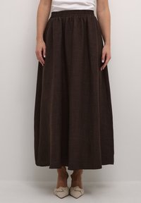 Jupe maxi marron fluide en tissu texturé, avec une taille élastique et une fente sur le côté, associée à des chaussures de couleur claire.