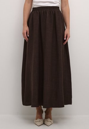 Jupe maxi marron fluide en tissu texturé, avec une taille élastique et une fente sur le côté, associée à des chaussures de couleur claire.