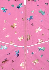 Veste rose avec des motifs de licornes brillants et de nœuds. Présente une fermeture éclair à l'avant et des accents blancs. Tissu doux avec une texture lisse.