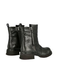 Botines negros de cuero con tacón apilado, que cuentan con una cremallera lateral y tachuelas decorativas a lo largo de la línea de la cremallera para mayor detalle.