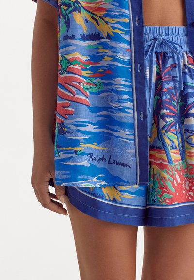 Set di camicia a maniche corte e pantaloni corti in tessuto blu con una stampa tropicale di palme e onde dell'oceano. Include un dettaglio del logo.