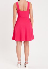 Vestido sin mangas rosa con un corsé ajustado, falda acampanada y tirantes anchos. Presenta una tela suave y un largo hasta mitad del muslo, combinado con tacones plateados.