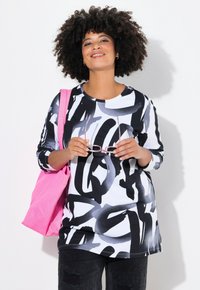 Maglietta a maniche lunghe in bianco e nero con scollatura rotonda, abbinata a jeans neri e una borsa tote rosa. Accessorio: occhiali tenuti in mano.