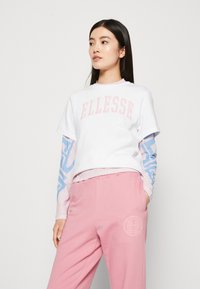 White cropped t-shirt with pink "ELLESSE" print, paired with pink sweatpants featuring a circular logo and light blue patterned long sleeves.