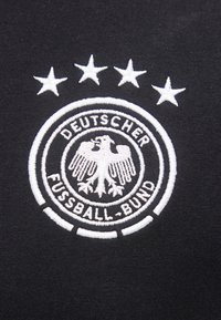 Κεντημένο λογότυπο της Γερμανικής Ποδοσφαιρικής Ομοσπονδίας σε μαύρο ύφασμα, με έναν αετό και τέσσερα αστέρια πάνω από το κυκλικό έμβλημα.