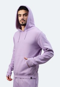 Felpa con cappuccio di colore viola chiaro, realizzata in materiale morbido. Presenta una tasca frontale, cappuccio con cordino e polsini a coste. Branding minimo sull'orlo.