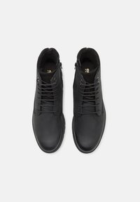 Botas de cuero negro hasta el tobillo con un acabado suave, diseño de cordones con seis ojetes y cremalleras laterales para facilitar su uso. Forro suave y texturizado visible en el interior.