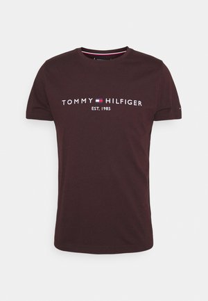 Tummanpunainen puuvillapaita, jossa on valkoisella ja punaisella tekstillä "TOMMY HILFIGER EST. 1985". Lyhyet hihat, pyöreä kaula-aukko ja sileä pinta.