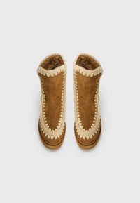 Stivaletti alla caviglia in suede marrone con rifiniture scallop color crema, foderati in pelliccia e con design della punta arrotondata, caratterizzati da suole sovrapposte per il massimo comfort.