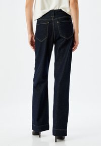 Jeans a gamba larga in denim scuro con design a cinque tasche, cuciture a contrasto e vita alta. Tessuto liscio e taglio dritto fino alla caviglia.