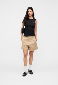 Μαύρο αμάνικο τοπ συνδυασμένο με μπεζ σορτς. Το μοντέλο φοράει μαύρα μοκασίνια, λευκές κάλτσες και κρατάει μια μικρή μαύρη τσάντα χειρός. Απλός σχεδιασμός.