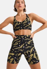 Black sports bra and high-waisted shorts featuring a pattern of green ferns and purple dots. Material appears stretchy and smooth.