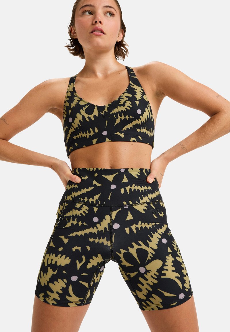 Black sports bra and high-waisted shorts featuring a pattern of green ferns and purple dots. Material appears stretchy and smooth.