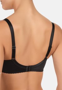 Reggiseno nero in tessuto liscio, con spalline regolabili e un bordo decorativo a scallop. Presenta una chiusura con gancio e occhiello sul retro.