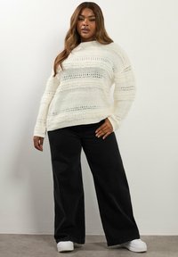 Biały sweter dzianinowy z fakturowanymi paskami, długimi rękawami i luźnym krojem, połączony z szerokimi czarnymi spodniami i białymi sneakerami.
