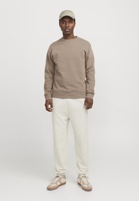 Sweatshirt i lysebrun, rund hals, med ribbede manchetter. Cremefarvede tapered bukser. Beige sneakers med tekstureret detaljer. Blødt stof generelt.