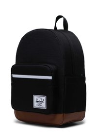 Zaino in tessuto nero con parte superiore arrotondata, tasca frontale con zip, cerniera bianca e fondo in pelle marrone. Presenta un patch con logo sulla parte anteriore.