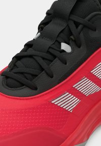 Gros plan d’une chaussure de sport rouge et noire avec des lacets noirs et un motif rayé blanc sur le côté.