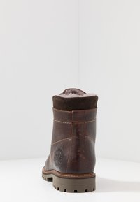 Botín de cuero marrón con suave forro de ante marrón, costuras visibles, suela de goma baja y detalle de logo embosado en el lateral.