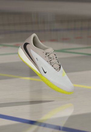 Ein einzelner beiger und weißer Nike-Sportschuh mit leuchtend gelber Sohle schwebt über dem Hallenboden mit farbigen Linien.