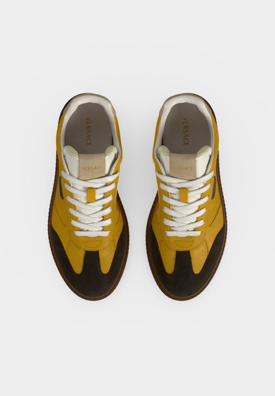 Paire de baskets en cuir jaune et noir avec des lacets blancs, une languette beige et le logo Versace à l'intérieur du talon, vue de dessus.