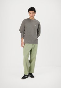 Grå langermet t-skjorte med en liten hvit logo, kombinert med løse lys grønne bukser og svarte sneakers med hvite striper.