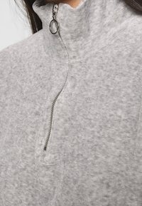 Grå zip-up fleece-tröja med hög krage, med en silverfärgad dragkedja och ett mjukt, strukturerat tyg.