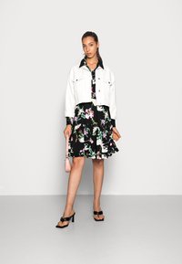 Jaqueta de ganga branca cortada sobre um vestido preto com padrões florais e mangas curtas, combinada com sandálias pretas e uma mala cruzada rosa claro.