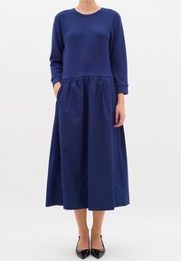 Mörkblå klänning med långa ärmar och samlad midja. Tillverkad av ett mjukt material, har den sidofickor och en helskuren kjol.