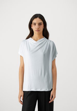 Top azzurro chiaro a maniche corte con scollatura drappeggiata. Realizzato in un tessuto morbido, presenta una vestibilità rilassata e una superficie liscia. Abbinato a pantaloni neri plissettati.