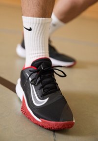 Černá sportovní bota s červenými akcenty, texturovaný materiál, bílý logo swoosh a černé tkaničky. Nosit s vroubkovanou bílou ponožkou.