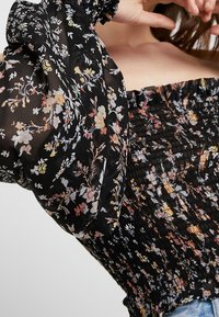 Black floral blouse with smocked body and puffed sleeves; features multicolored flower patterns on sheer material.
