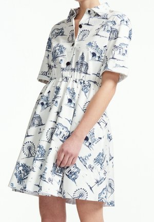 Robe blanche à manches courtes avec col et boutons noirs, ornée d'illustrations bleues d'architecture et de grande roue, coupe ample.