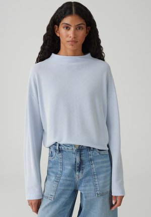 Lichtblauw shirt met lange mouwen en een gestructureerd patroon, hoge halslijn, losse pasvorm, gecombineerd met lichtblauwe jeans met hoge taille.