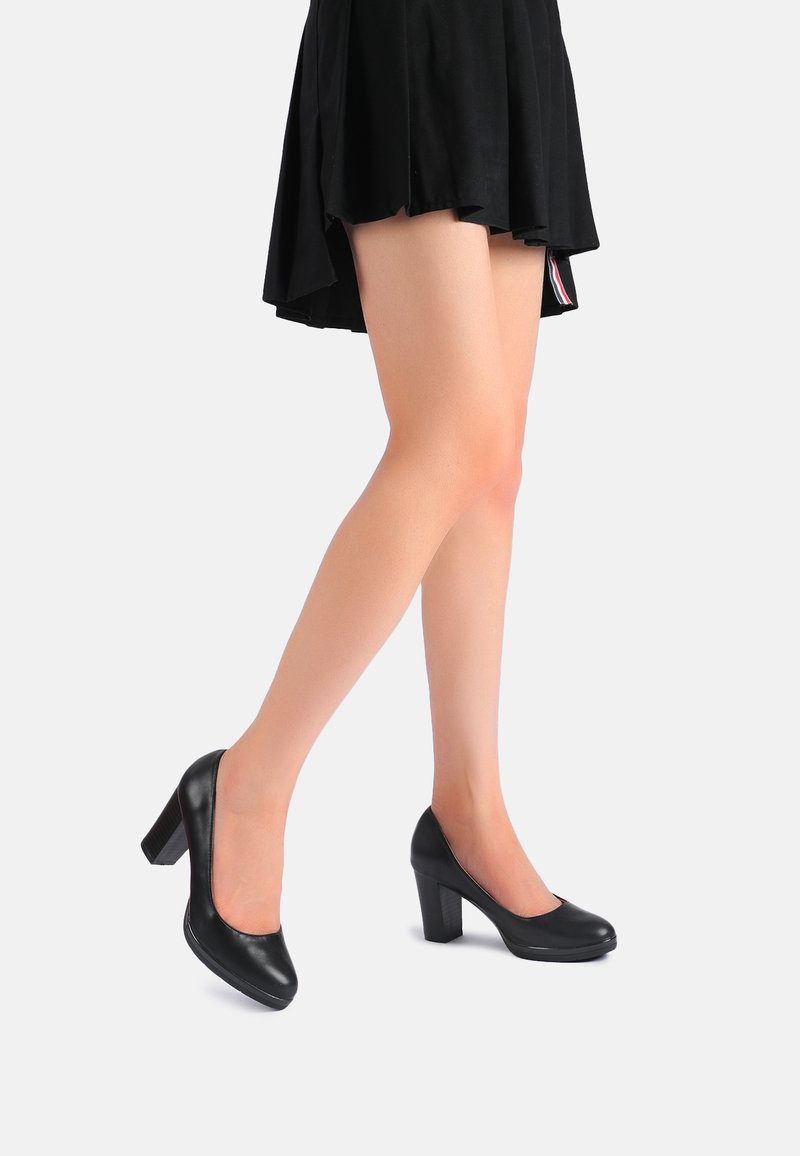 Decollete nere in pelle con punta arrotondata, tacco a blocco strutturato e finitura liscia. Indossate con una gonna nera, gambe parzialmente visibili.