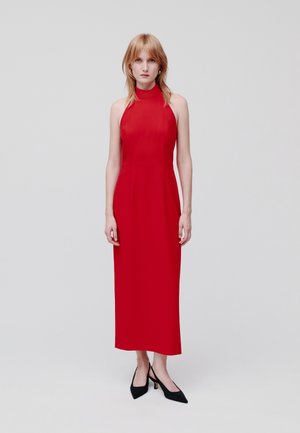 Rode halterneck midi-jurk met een aansluitende lijfje en een rechte silhouet, met een gladde textuur en minimale accessoires. Zwarte puntige hakken.