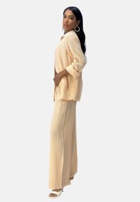 Licht perzikkleurige twee-delige outfit met een gestructureerde, loszittende blouse met opgerolde mouwen en eenwijde broek in een vergelijkbare stof.