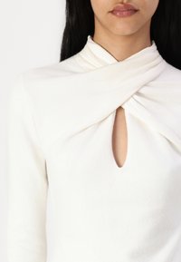Cream-colored knit top featuring a folded collar design and a center keyhole opening. Soft texture with long sleeves.
