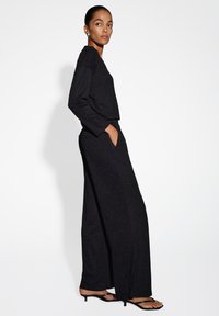 Tutina nera a gamba larga con maniche lunghe, realizzata in un materiale testurizzato, con una leggera scintilla e tasche laterali. Regolabile per una vestibilità perfetta.