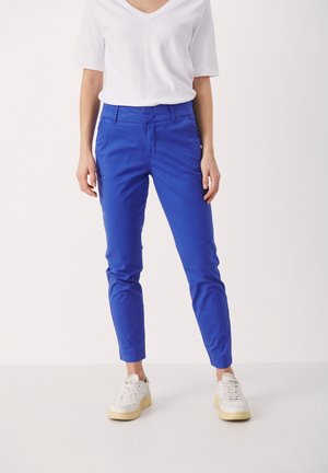 Pantalon en coton bleu avec une coupe slim, doté de poches avant et d'une fermeture éclair. Associé à un t-shirt blanc à col en V et des baskets blanches.