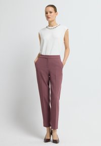 Witte mouwloze top met een met juwelen versierde halslijn, gecombineerd met slanke bordeauxkleurige broeken. Voltooi de look met bruine puntige hakken.