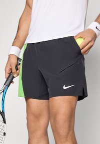 Μαύρο αθλητικό σορτς με πράσινη λεπτομέρεια, κατασκευασμένο από ελαφρύ ύφασμα, με πλαϊνή τσέπη και λευκό λογότυπο Nike στο μπροστινό μέρος.