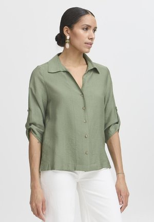 Blusa button-up morbida e testurizzata di un verde chiaro, con colletto e maniche a tre quarti, dotata di cuffie arrotolate e bottoni marroni.