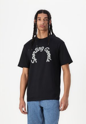 Sort bomulds t-shirt med en buet hvid "Sporting Goods" grafik på forsiden, korte ærmer og en afslappet pasform. Stylet med blå jeans.
