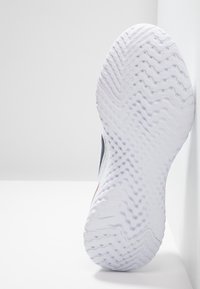 White athletic shoe sole with a textured zigzag pattern and small circular grips, angled against a plain background.