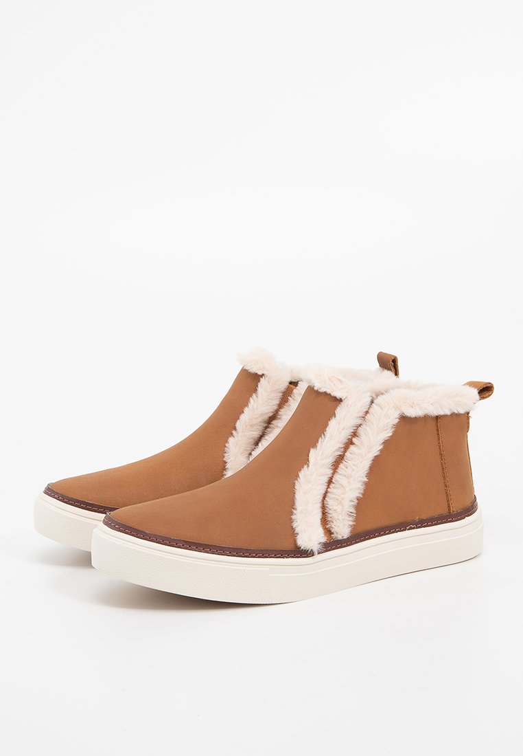 Bottines en simili cuir marron avec une doublure blanche duveteuse, présentant une tige lisse, une semelle blanche contrastante et des panneaux latéraux en élastique.