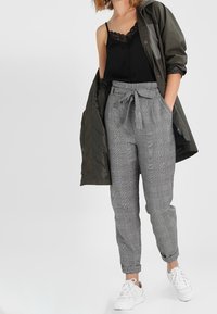Černá krajková košíková halenka, olivově zelená bunda, šedé kostkované kalhoty s vysokým pasem a bílé tenisky. Složení neformálního outfitu.