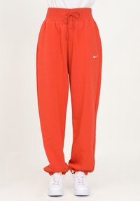 Pantalones de chándal rojos con una cinturilla elástica ancha y cordón. Presenta un logo de Nike en blanco y puños elásticos en los tobillos.